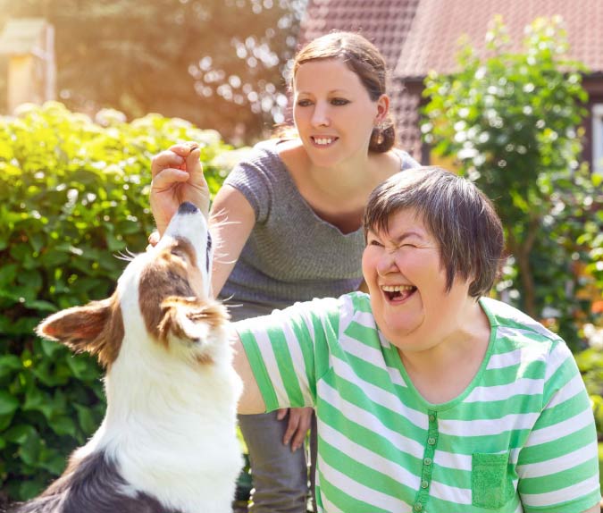 Caregiver and a woman with disabilities playing with a dog.